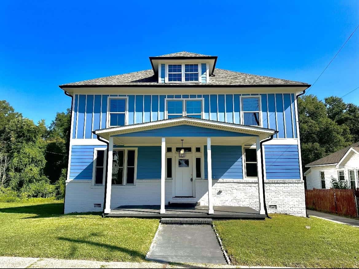 A two-story blue and white house with a centered front entrance and a small front yard under a clear blue sky.