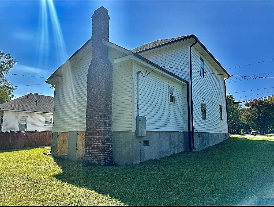 A two-story house with beige siding and a large brick chimney under clear blue skies.