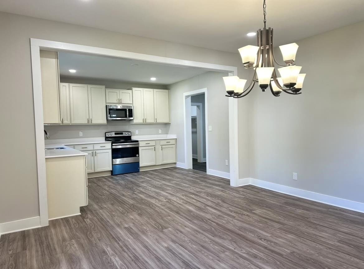 A modern kitchen with white cabinetry, stainless steel appliances, and wood laminate flooring, viewed from an adjacent room with a hanging chandelier.