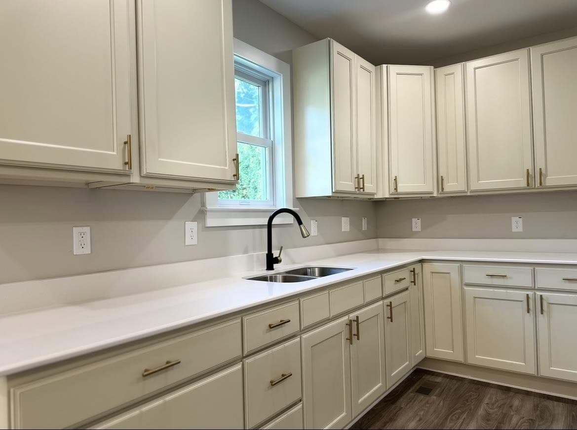 A modern kitchen with white cabinets, stainless steel sink, and granite countertops with a window overlooking the outdoors.