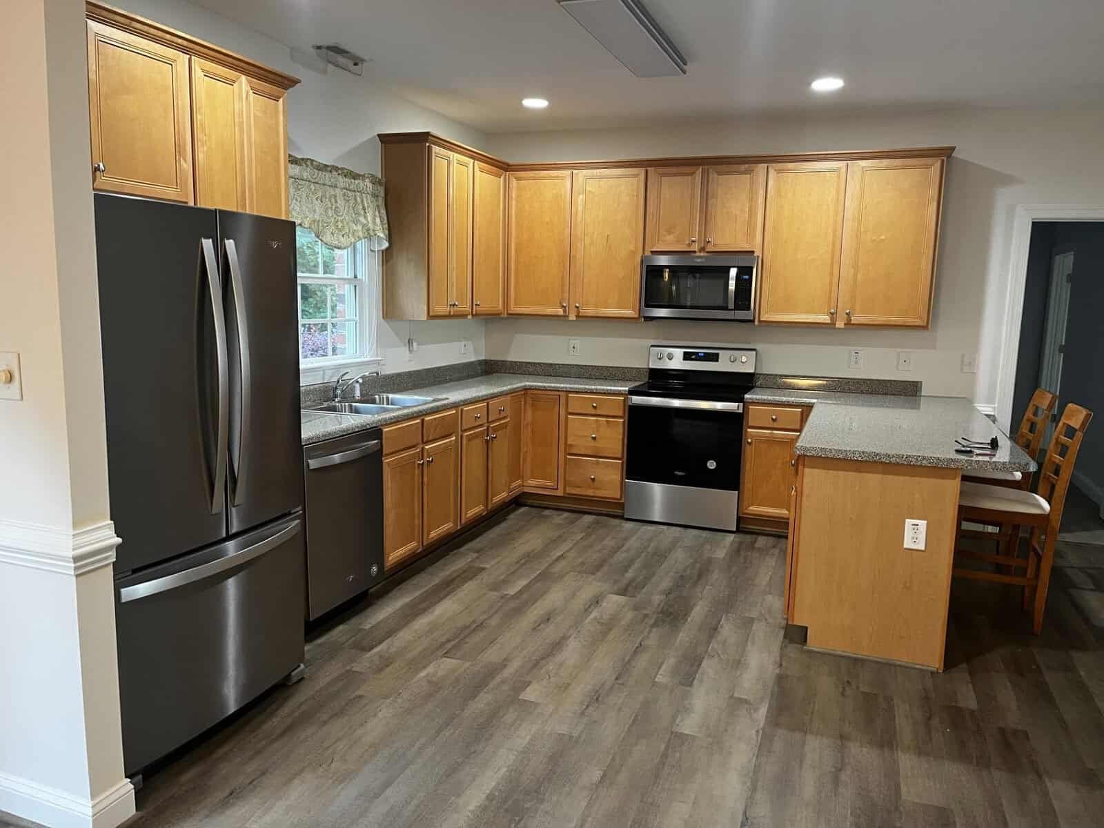 A modern kitchen with stainless steel appliances, wooden cabinets, and vinyl plank flooring.