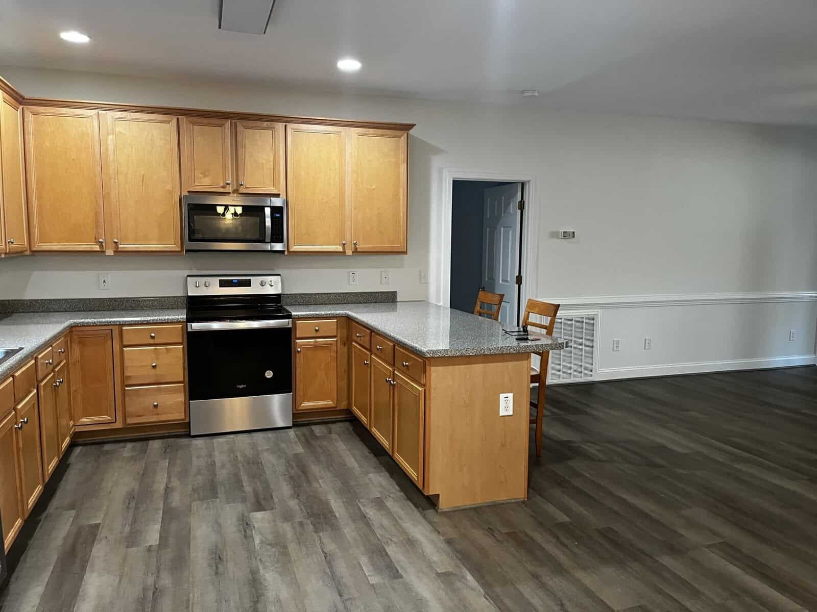 A modern kitchen with wooden cabinets, granite countertops, stainless steel appliances, and laminate flooring extending into an adjoining room.