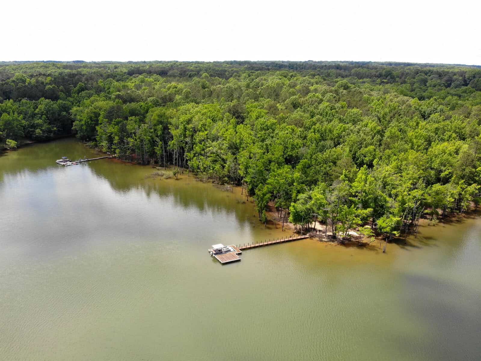 An aerial view of a calm lake with a floating dock surrounded by densely wooded shores.