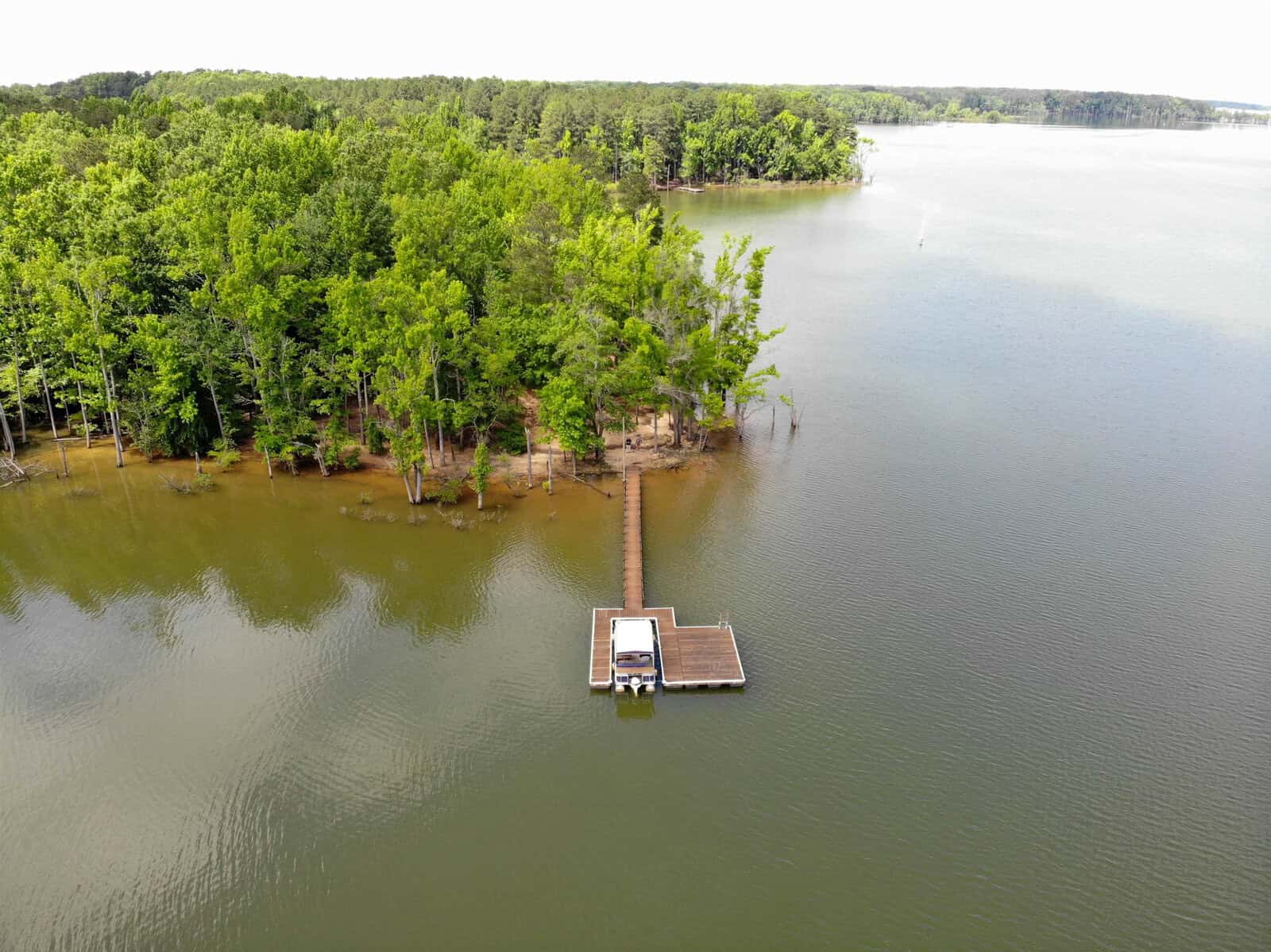 A small wooden dock is surrounded by water near a lush tree line at the edge of a calm lake.