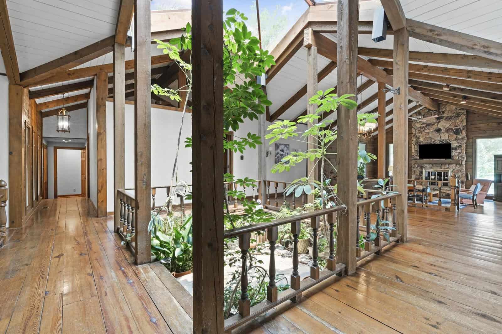 Interior of a spacious room with wooden floors and beams, featuring an abundance of potted plants and a living area with a television in the background.