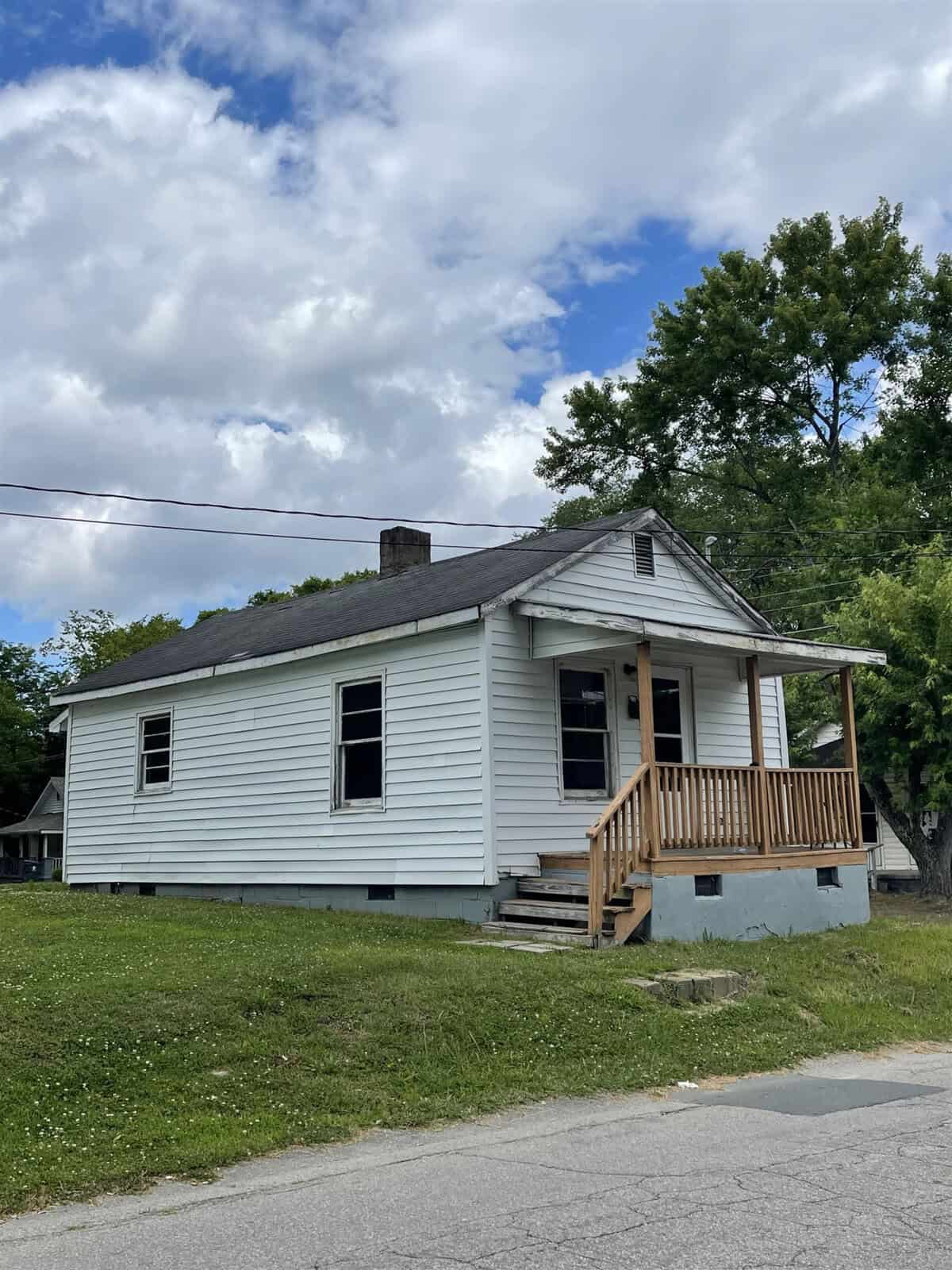 A small, white single-story house with a new wooden front porch under a cloudy sky.