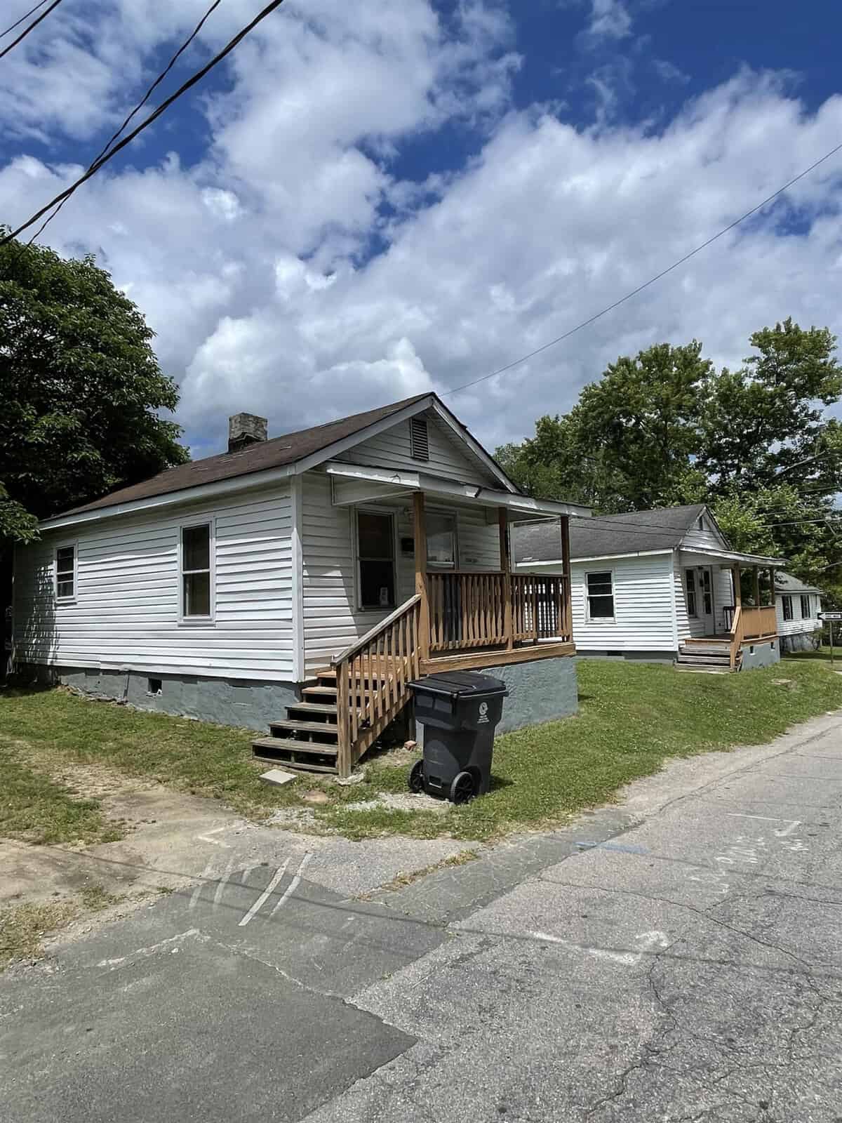 A house with a porch and a trash can on the side of the road.