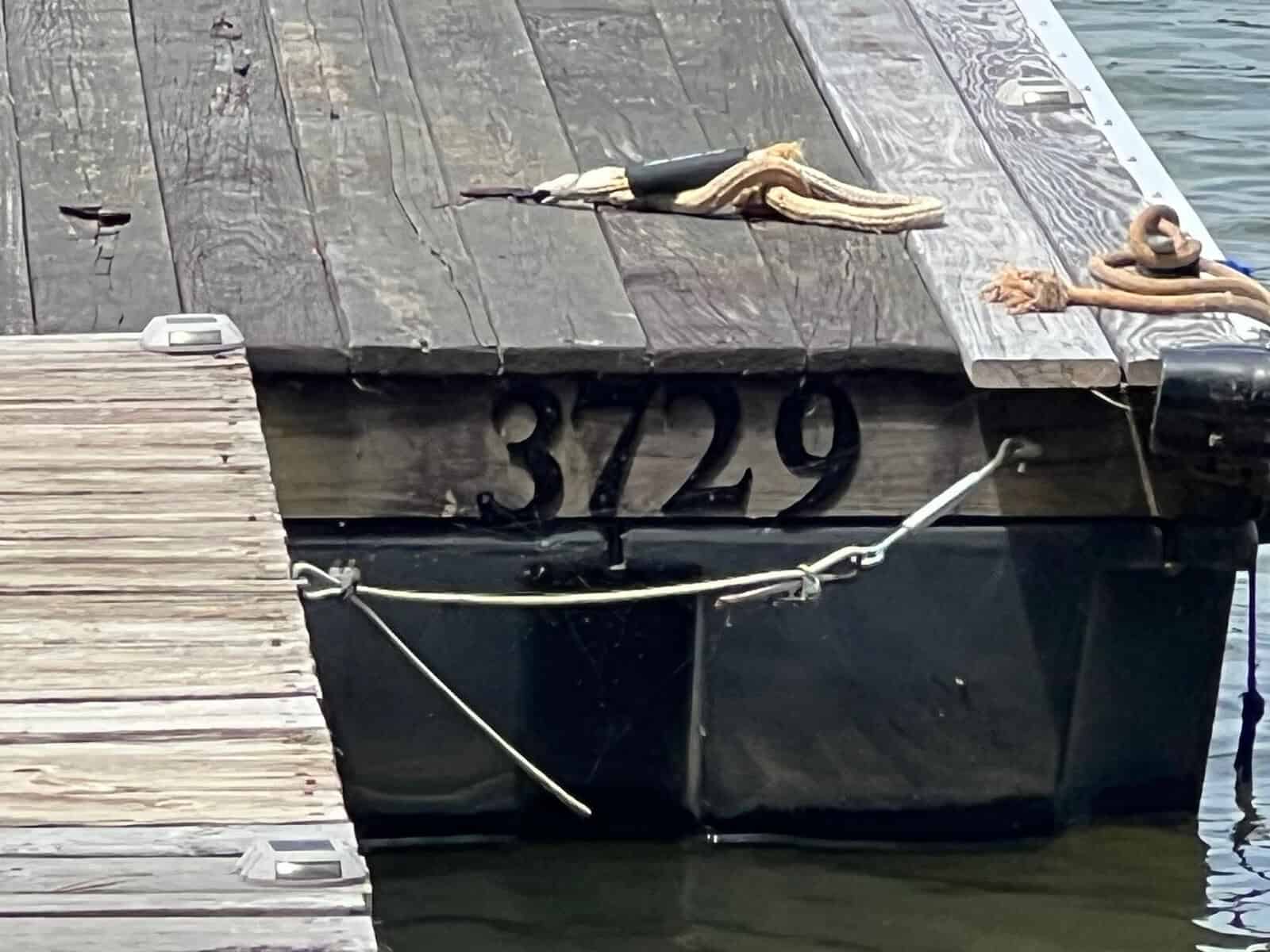 A wooden dock with the number "3729" painted on the side. Coiled ropes are visible on the surface, next to the water.