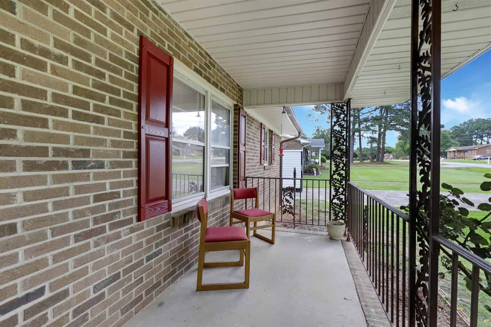 A brick house with a covered porch featuring two red chairs and a red door.