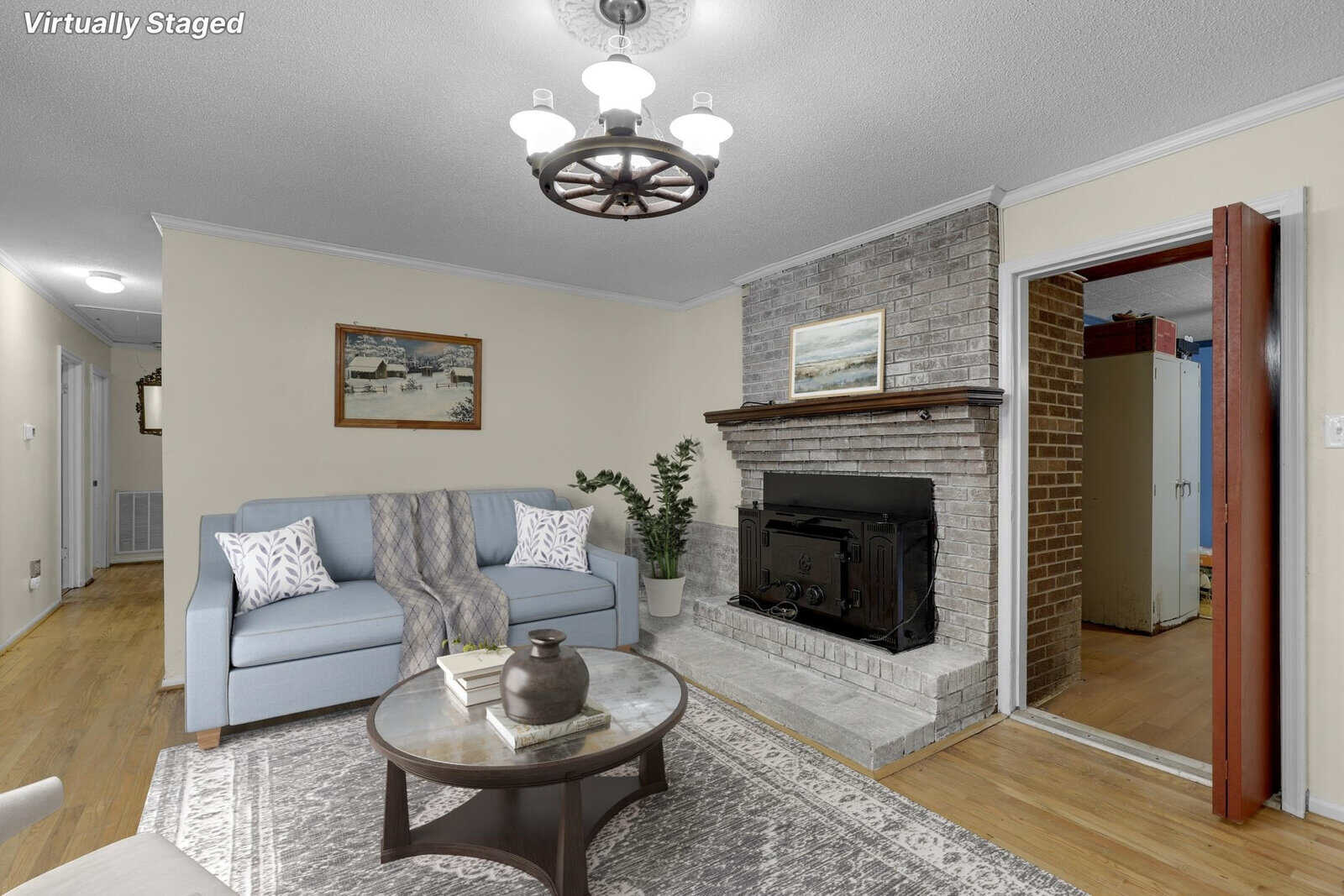 A neatly arranged living room featuring a gray sofa with decorative pillows, a glass-top coffee table, a fireplace, and a chandelier, with a note on the image indicating that the staging is virtual.