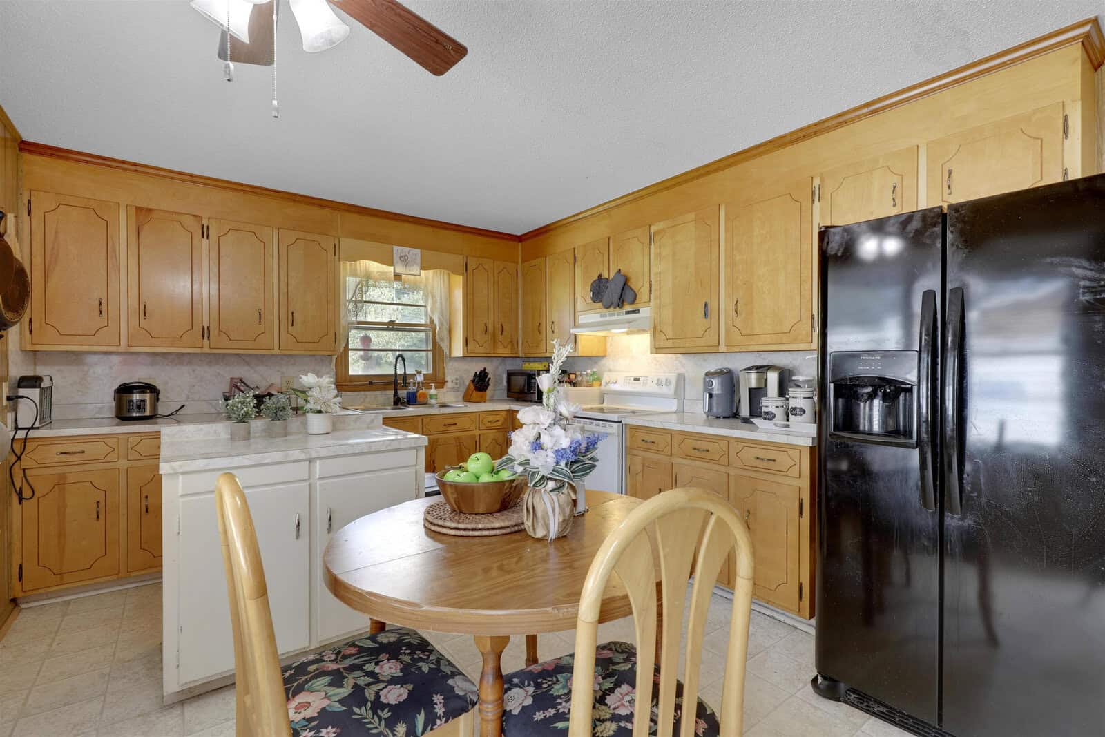 A traditional kitchen with wooden cabinetry, white appliances, and a dining table set near a window.