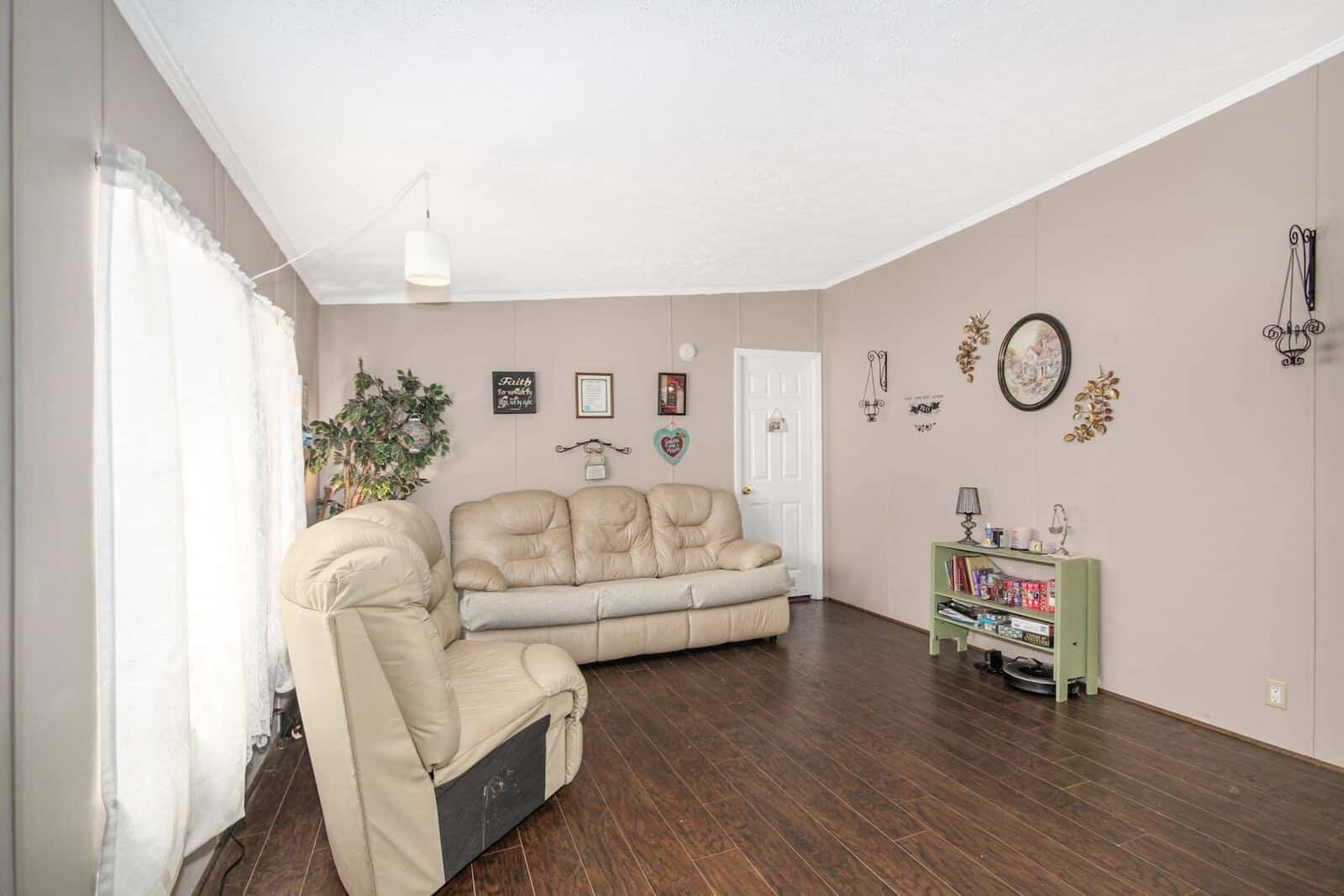 A well-lit, tidy living room featuring a beige leather sofa, dark wooden flooring, and walls adorned with various decorative items and picture frames.