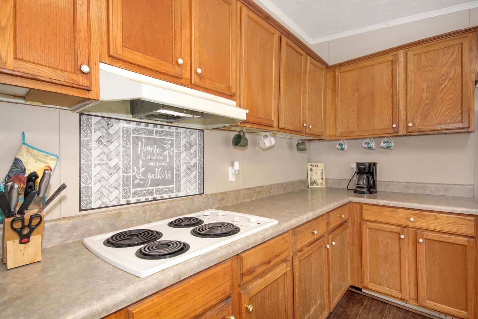 A well-used kitchen with wooden cabinets, a white stove top, and a decorative chalkboard sign above the hood.