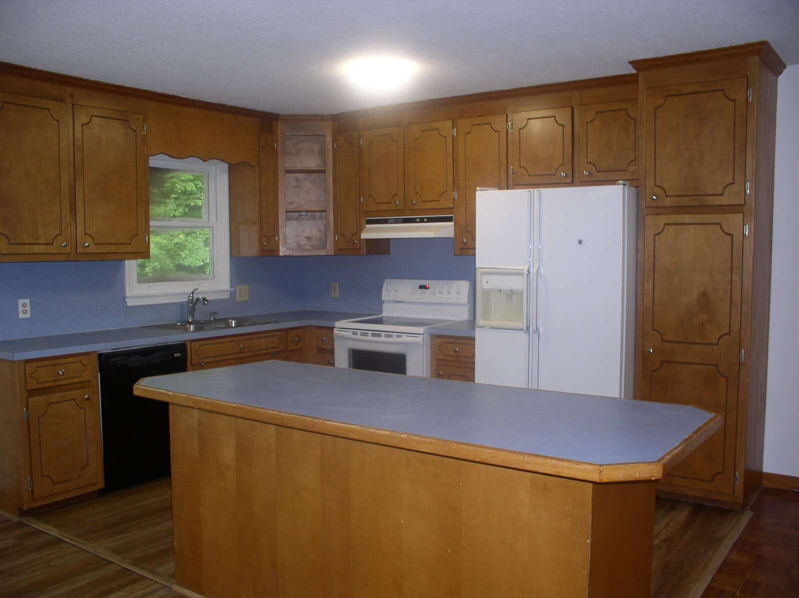 A spacious kitchen featuring wooden cabinetry, blue countertops, white appliances, and an island in the center.