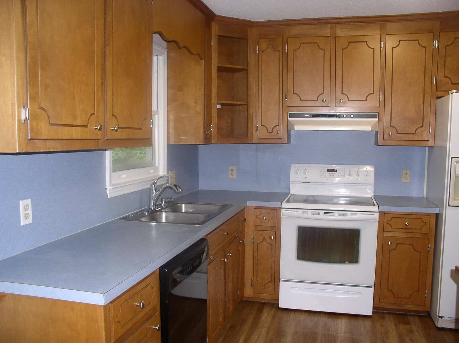 A kitchen with wooden cabinets, blue countertops, a double sink, and a white range oven.