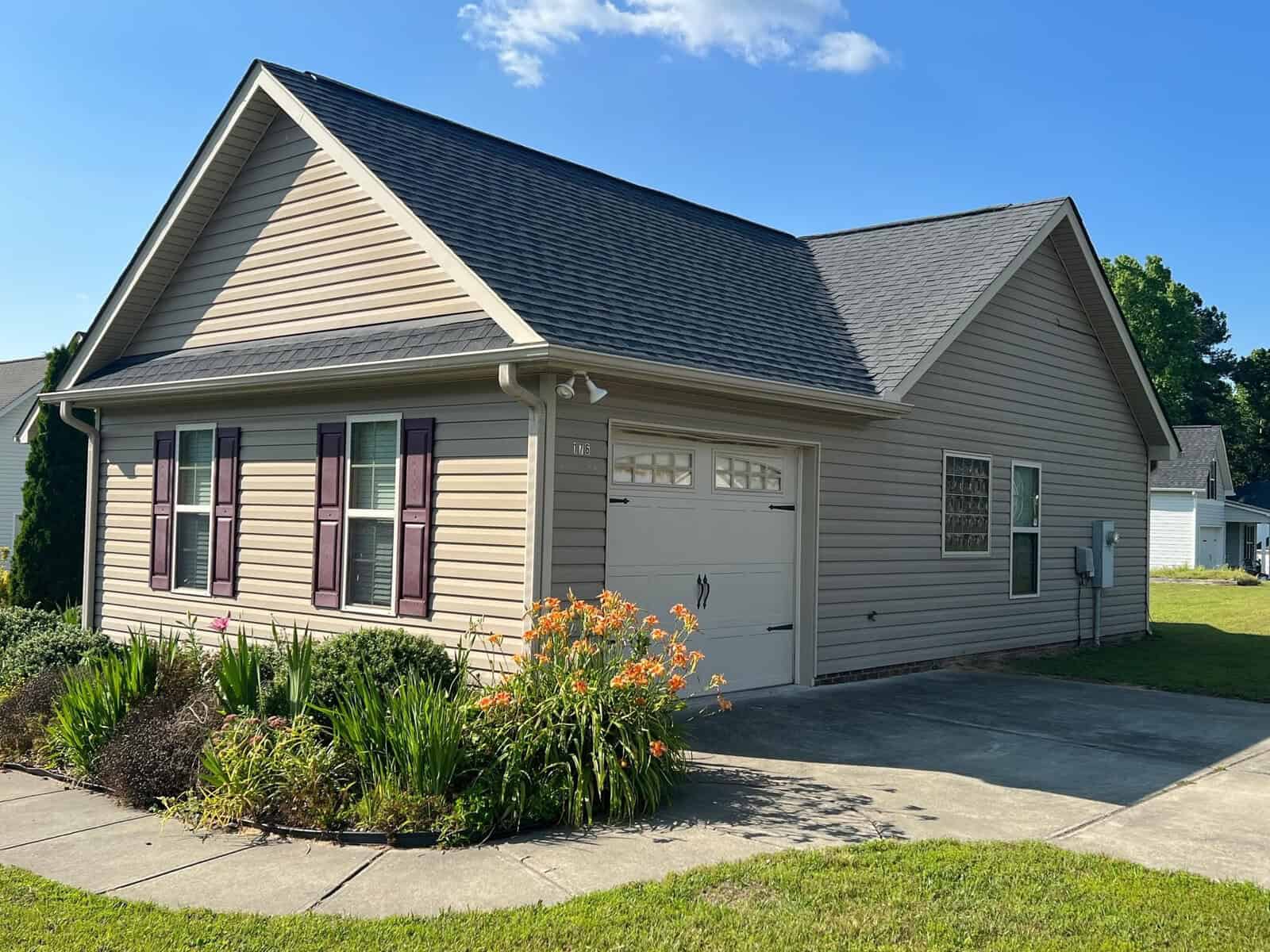 Single-story suburban house with beige siding, a double garage, and a manicured lawn with decorative plants.