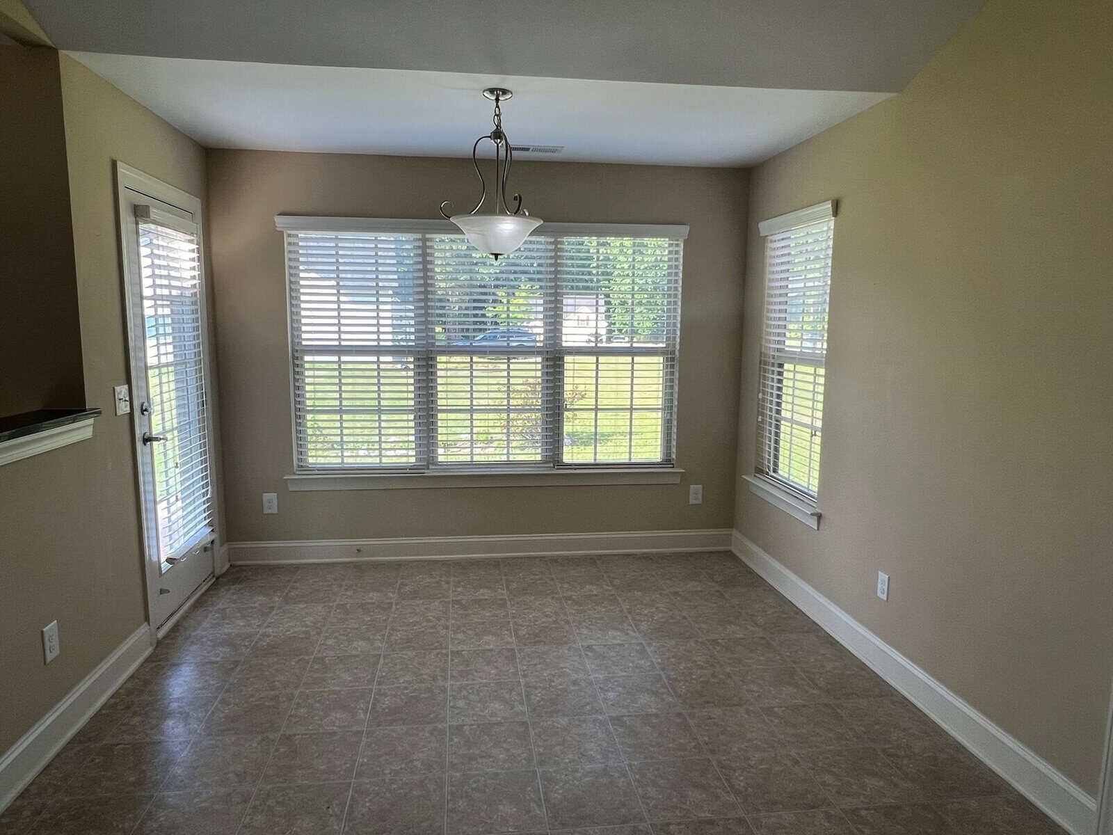 Empty room with tiled flooring, two windows with blinds, and a hanging light fixture.