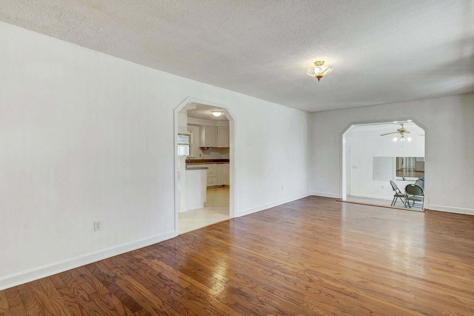 Empty living room with hardwood floors, white walls, and openings leading to adjacent rooms.