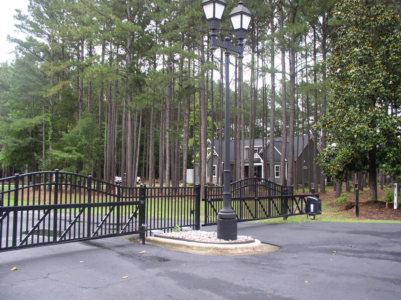 A gated entrance to a property with tall pine trees in the background and a streetlamp at the center.