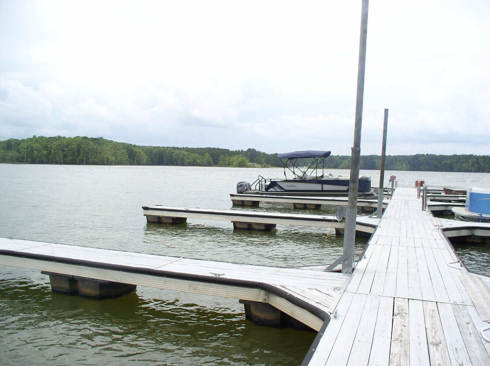 A wooden pier extending into a calm lake with moored boats under an overcast sky.