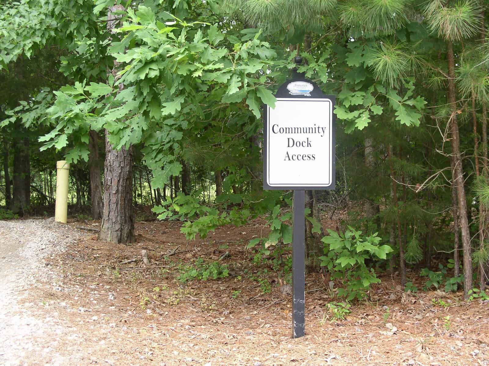 A signpost indicating "community dock access" located on the side of a gravel path nearby some trees.