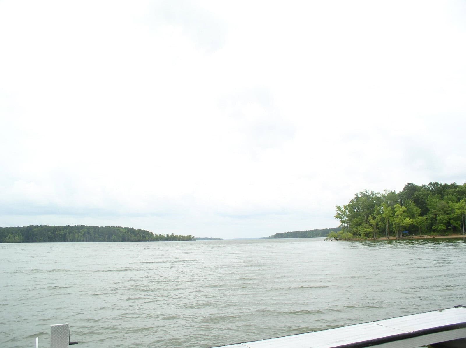 A lake with choppy water on an overcast day, viewed from a deck with a railing visible in the lower right corner.