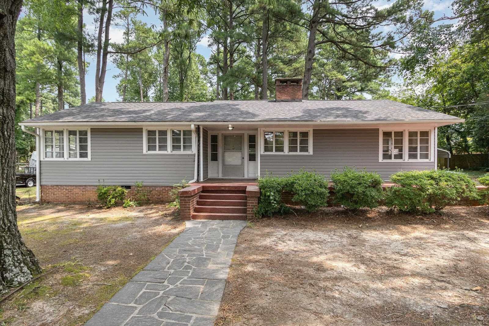 A single-story residential house at 120 Cedarwood Drive, Henderson NC, with gray siding and a gabled roof, features a central front door with flanking windows, a brick staircase, and