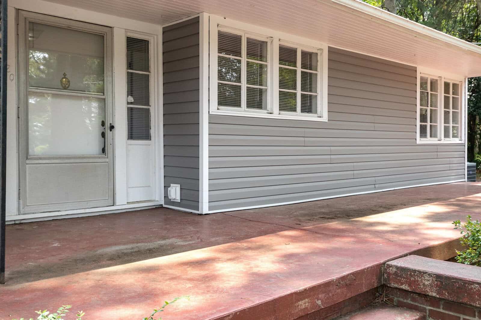 A front view of a house with a red concrete porch, a white screen door, and gray siding.