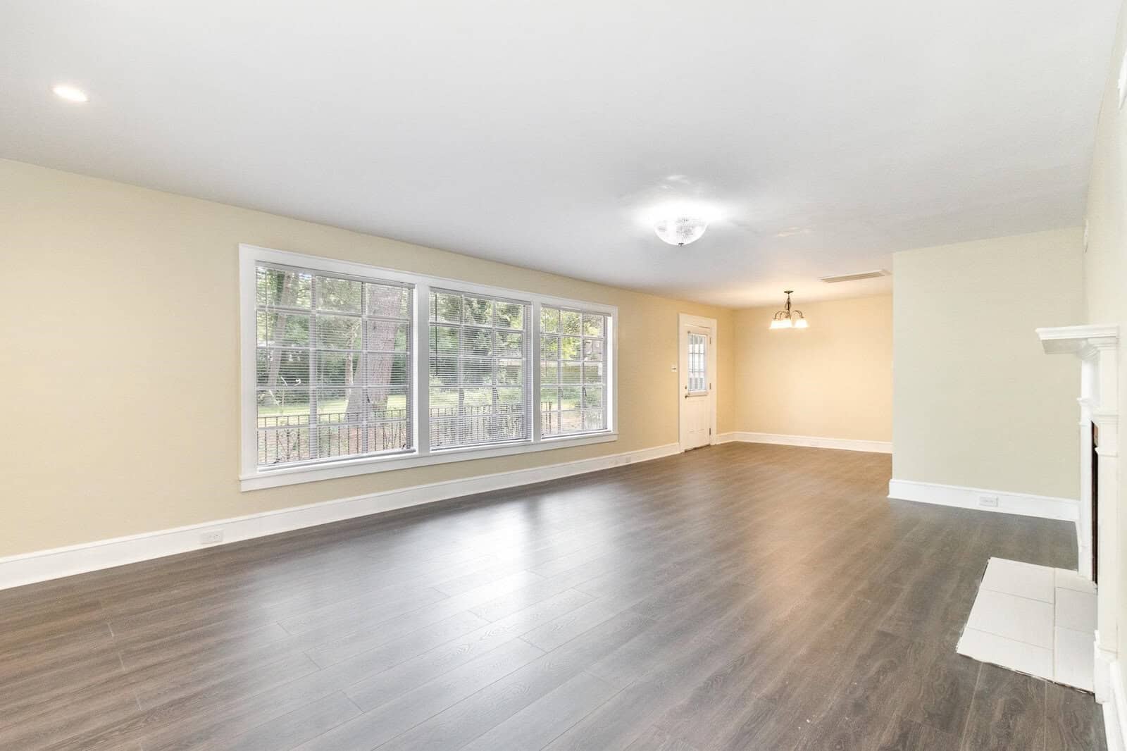 An empty room with laminate flooring, off-white walls, and a row of windows offering a view of a yard with a fence.
