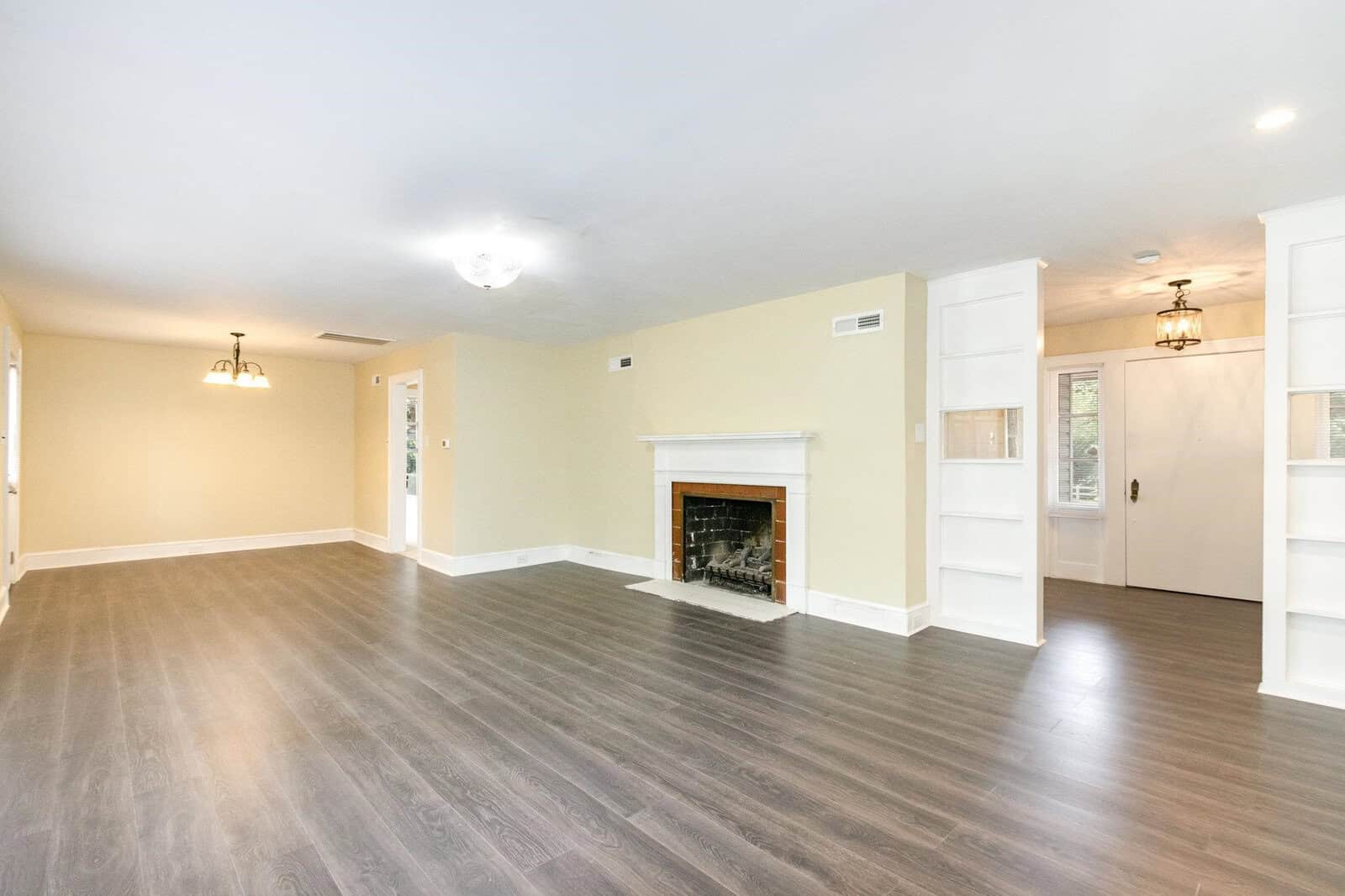 A spacious room with laminate flooring, a fireplace, white walls, and multiple light fixtures.