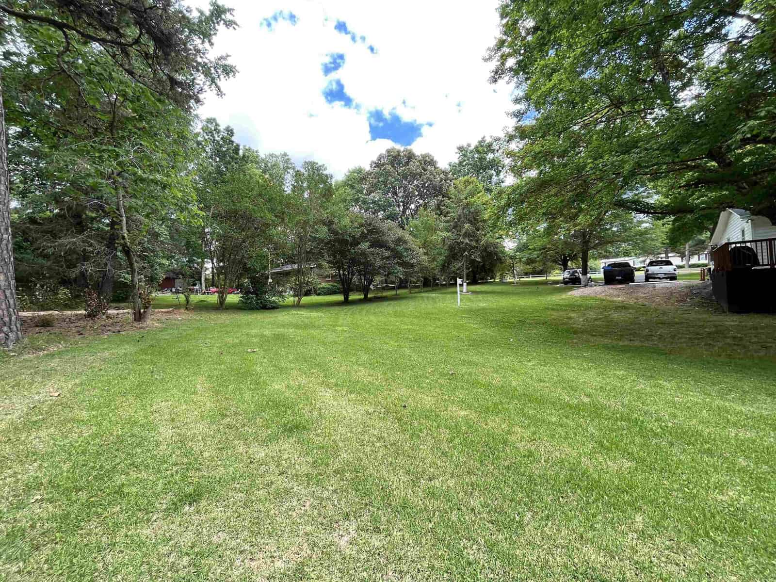 A well-maintained grassy area with trees in a suburban or park setting on a sunny day.