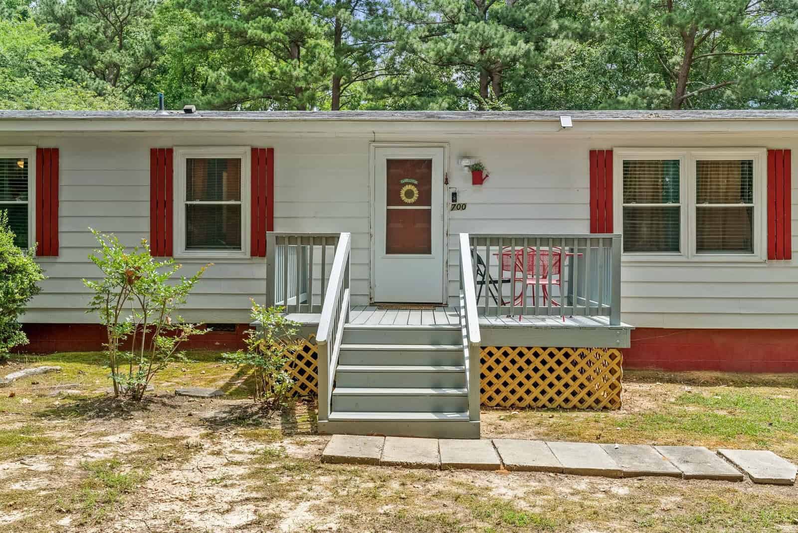 A single-story home with white siding and red shutters featuring a small porch with steps leading to the front door.
