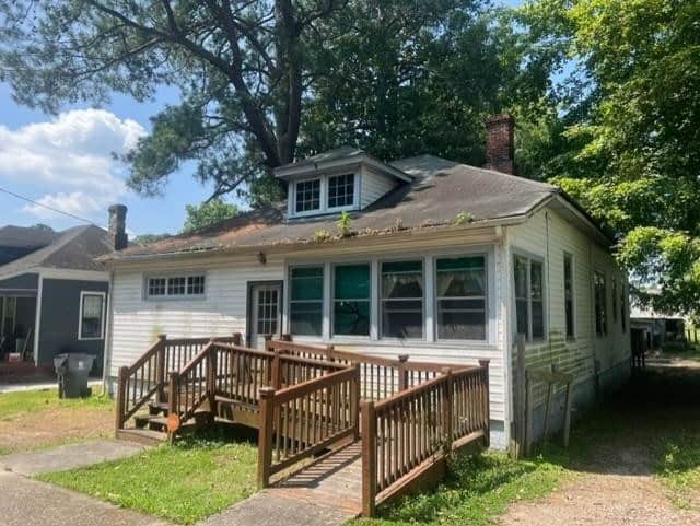 A single-story, white house with green shutters and a wooden front deck under a clear blue sky.