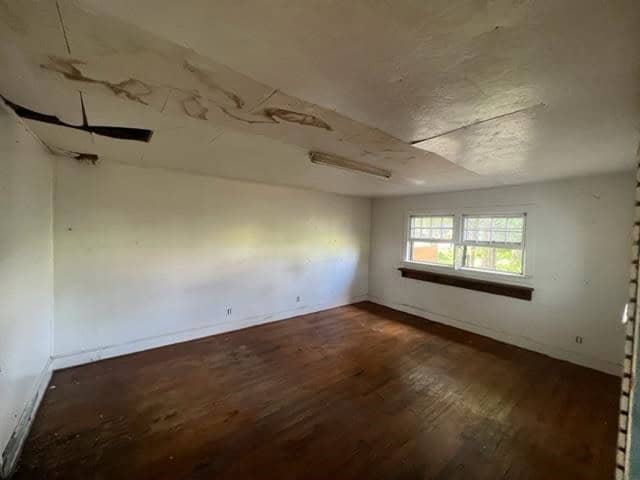 An empty room with hardwood flooring, a window, and signs of ceiling damage.