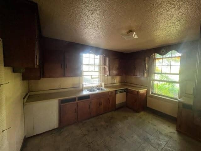 An old, empty kitchen with worn wooden cabinets, a sink, and no appliances, illuminated by natural light from windows. the room appears to need renovation.