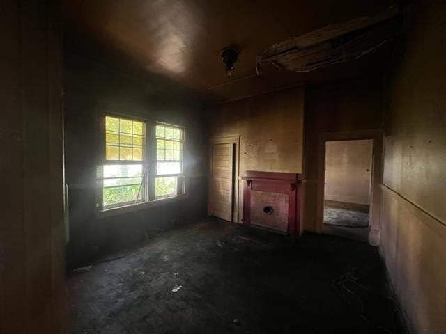 A dimly lit, vacant room with worn-out walls, a fireplace, and a window with yellow-tinted glass panes.