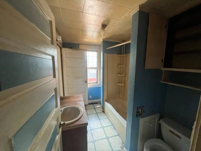 A dated bathroom with blue walls, a white shower unit, and built-in shelving, exhibiting signs of wear and potential need for renovation.