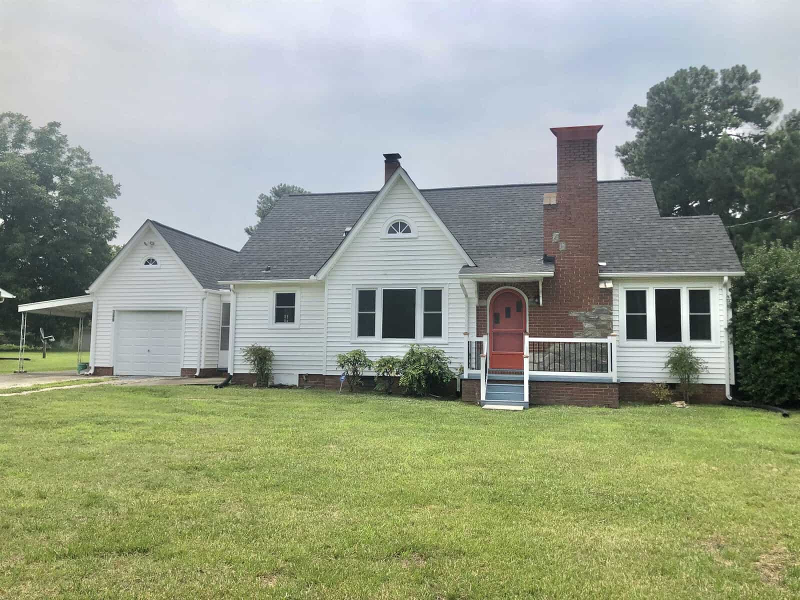 A white single-story house with a gabled roof featuring a red front door and an attached garage situated on a grassy lawn at 306 Bearpond Road, Henderson NC.