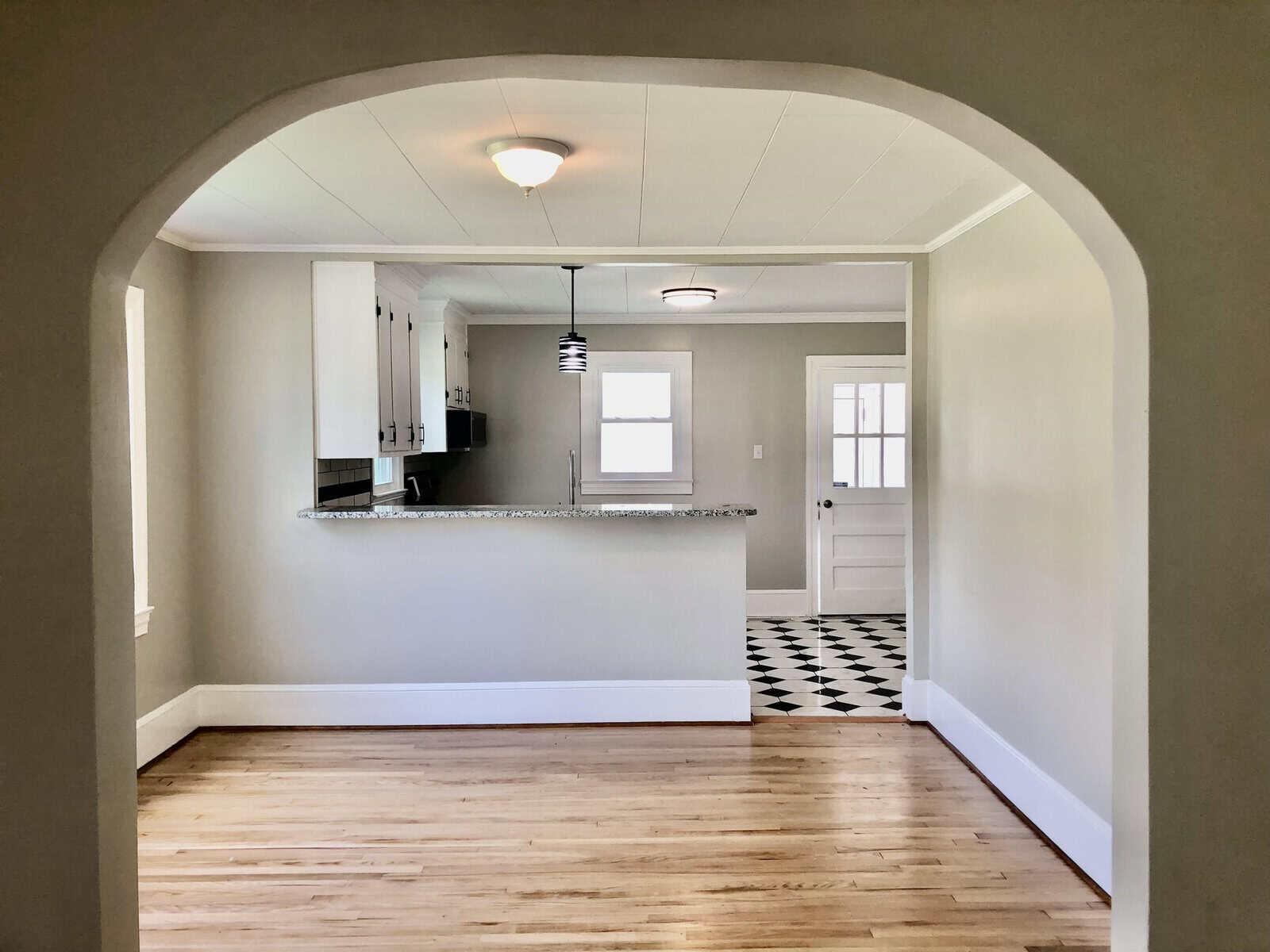 An archway leading to a neatly arranged kitchen with a breakfast bar, viewed from an adjoining room with hardwood floors.