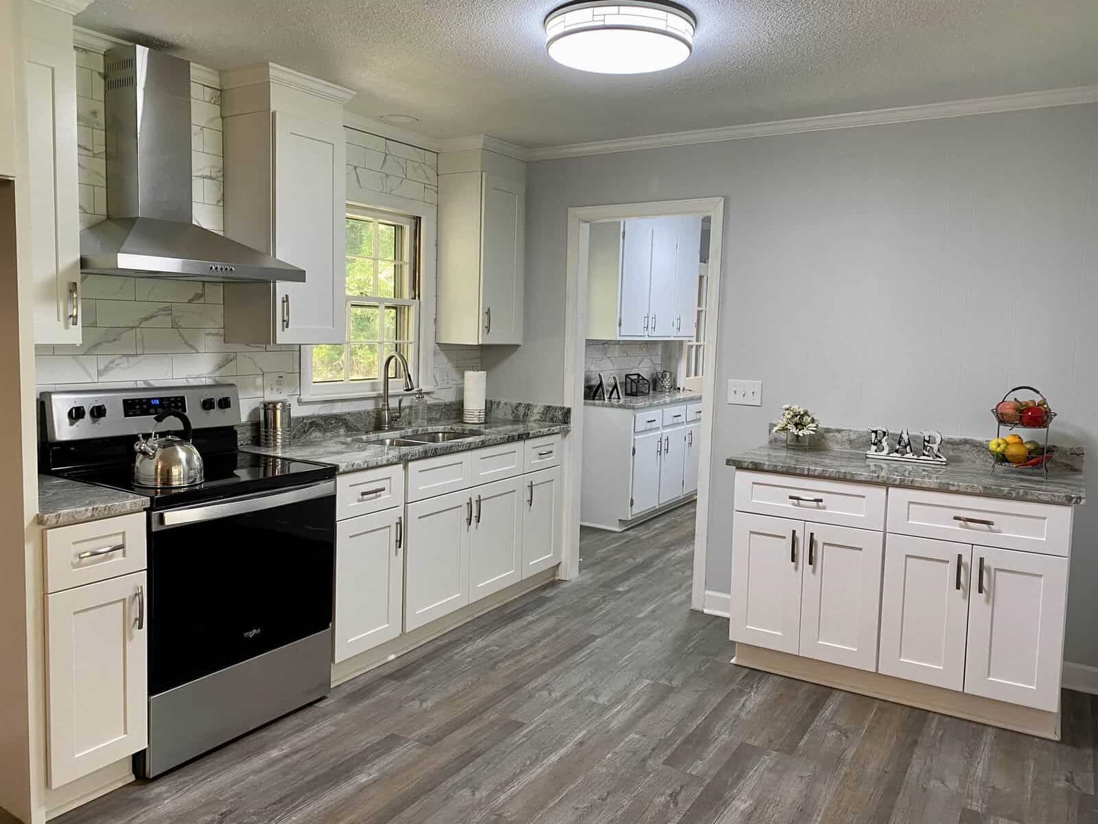 A modern kitchen with white cabinetry, stainless steel appliances, and grey flooring.