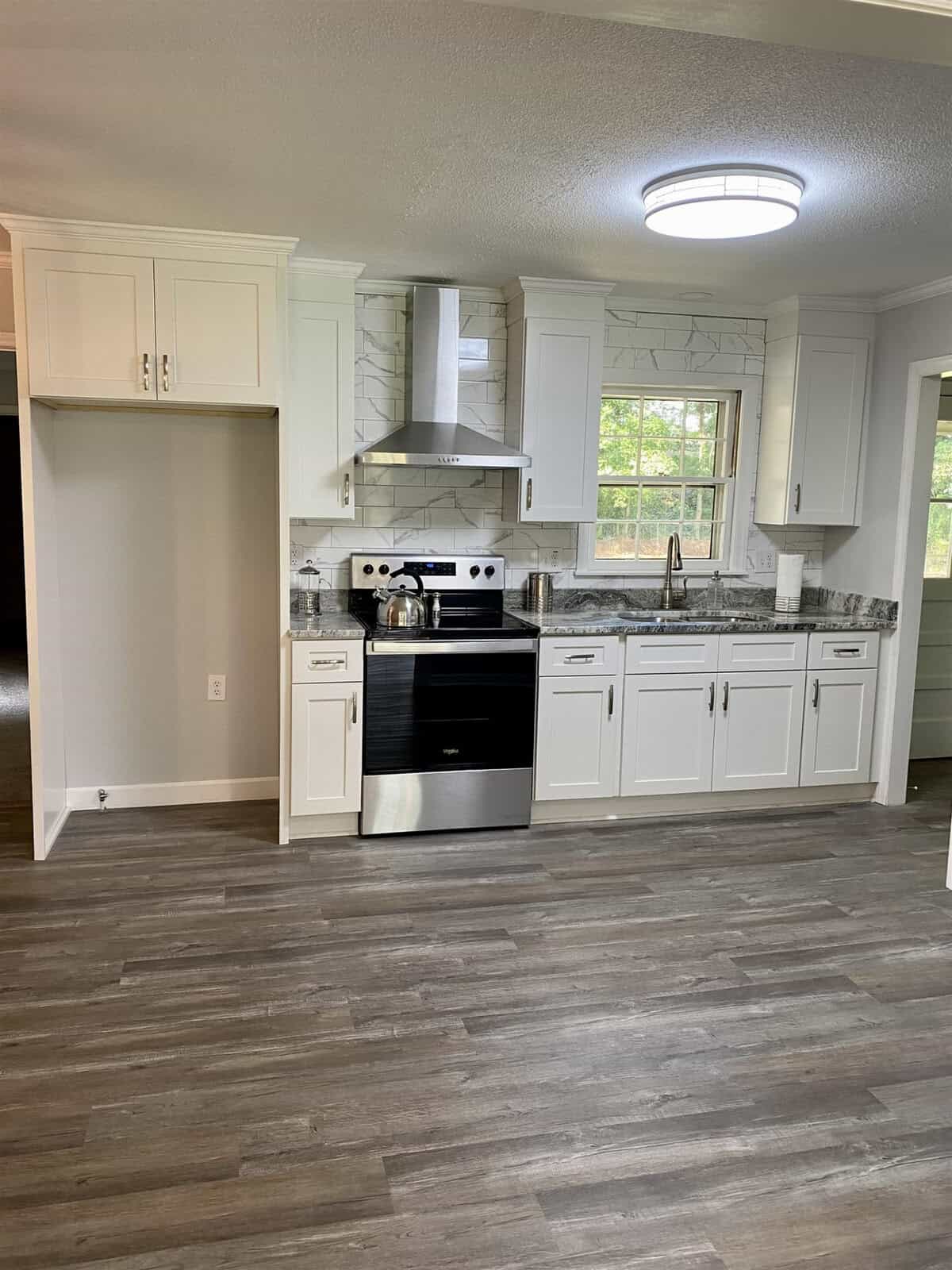 A modern kitchen with white cabinetry, stainless steel appliances, and gray wood-patterned flooring.