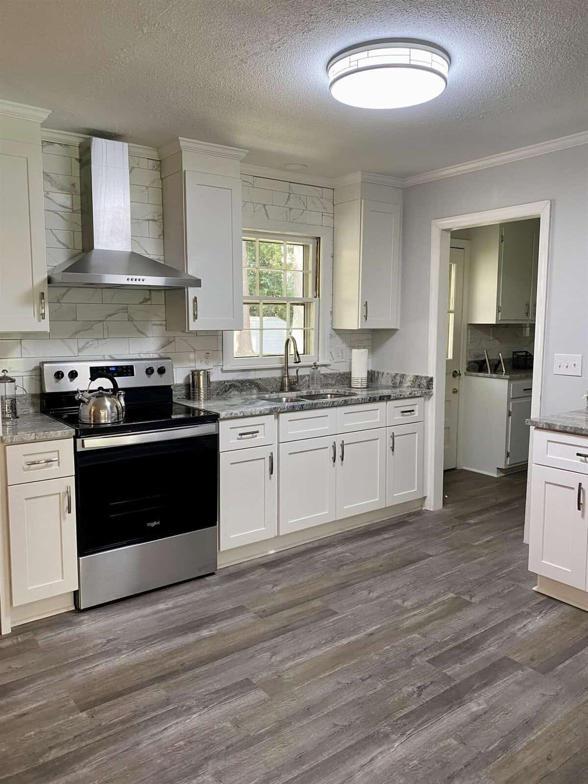 A modern kitchen with white cabinetry, stainless steel appliances, marble countertops, and gray laminate flooring.