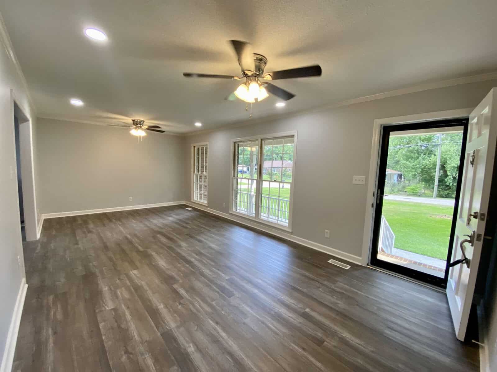 An empty room with gray flooring, white walls, multiple ceiling lights, and a ceiling fan, featuring a glass sliding door leading to an outside area with a metal fence.