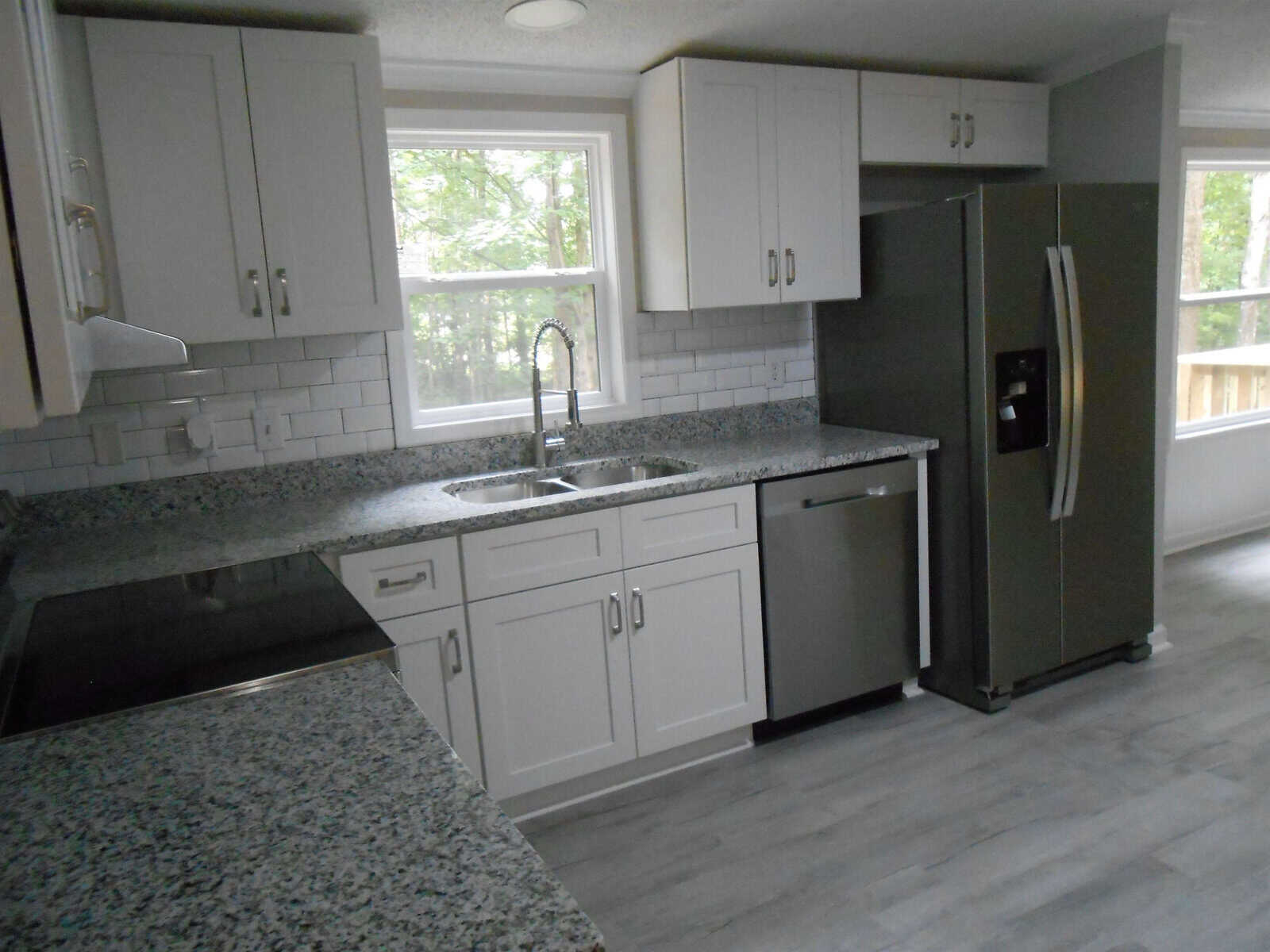 A modern kitchen with grey granite countertops, white cabinets, a stainless steel refrigerator, and a window above the sink providing natural light.