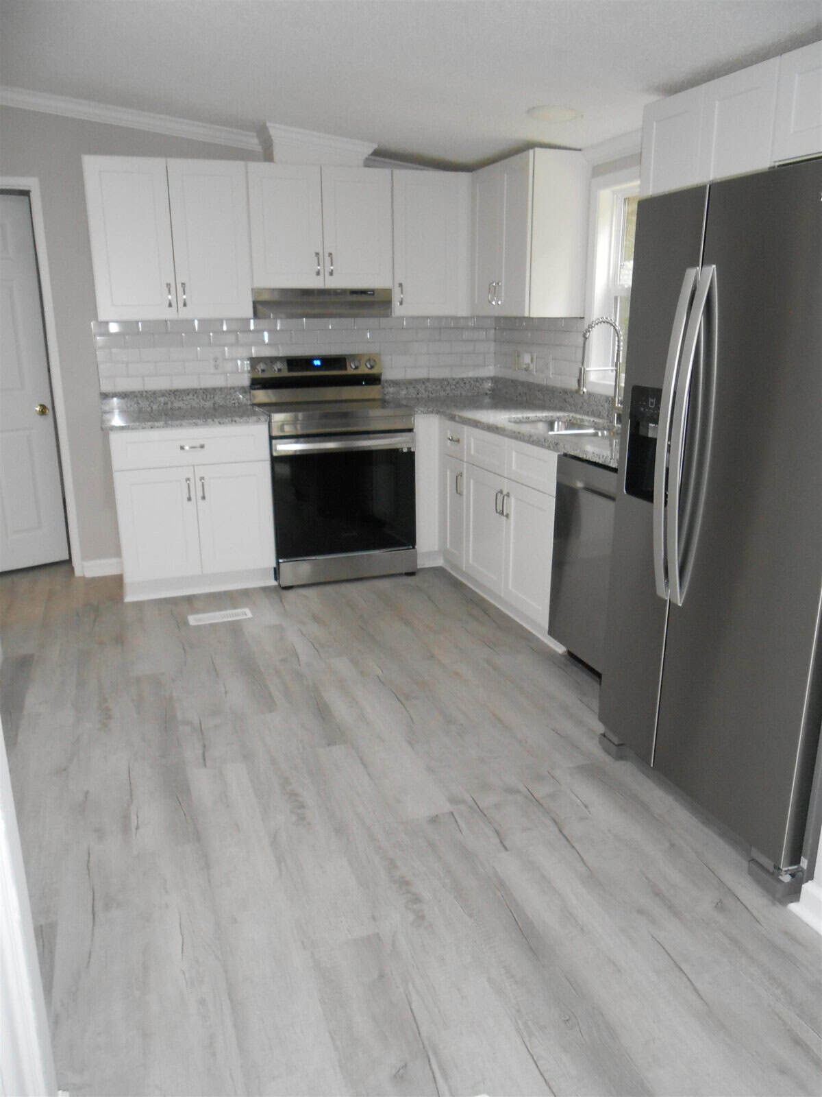 A modern kitchen with white cabinets, stainless steel appliances, and light gray wood flooring.