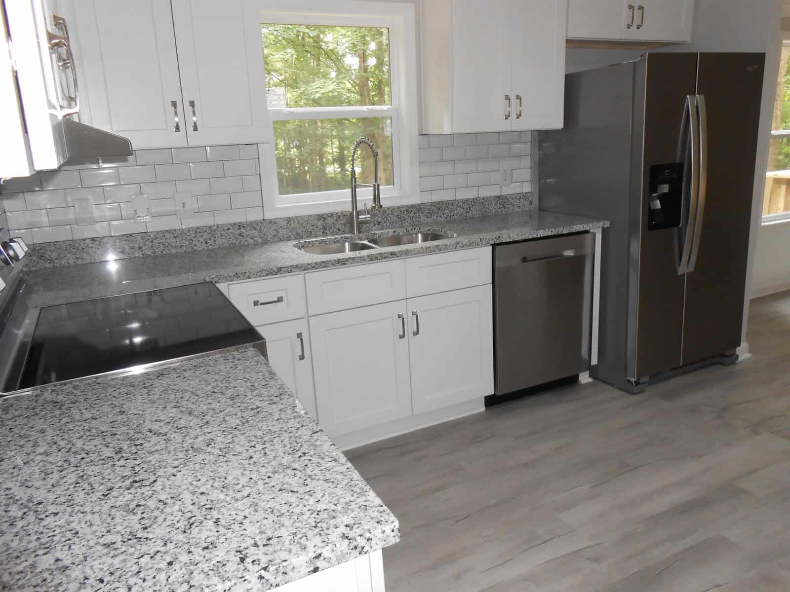 A modern kitchen with white cabinetry, stainless steel appliances, granite countertops, and gray tile backsplash.