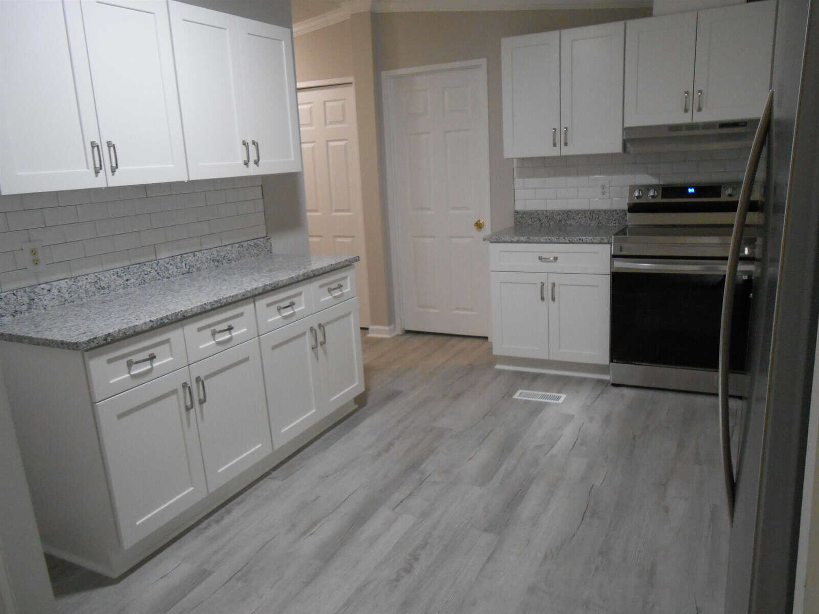 A modern kitchen interior with white cabinetry, granite countertops, and stainless steel appliances with vinyl flooring.