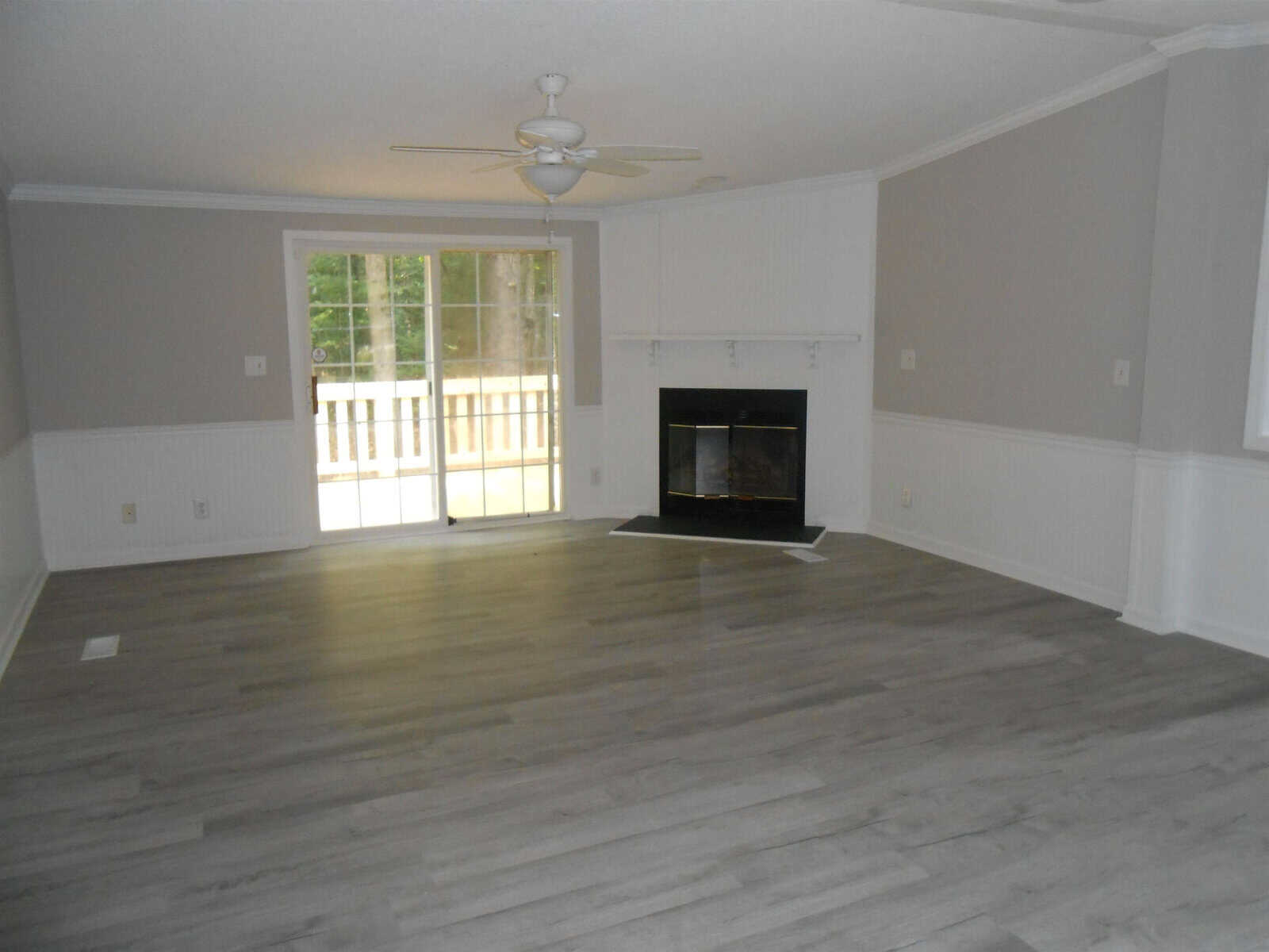 An empty room featuring a hardwood floor, a fireplace with a black hearth, a ceiling fan, and sliding doors leading to an outdoor area.