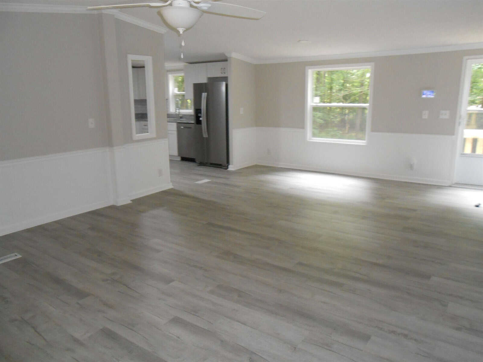 Empty room with gray flooring, white walls with chair rail molding, a ceiling fan, and a stainless steel refrigerator in the corner.