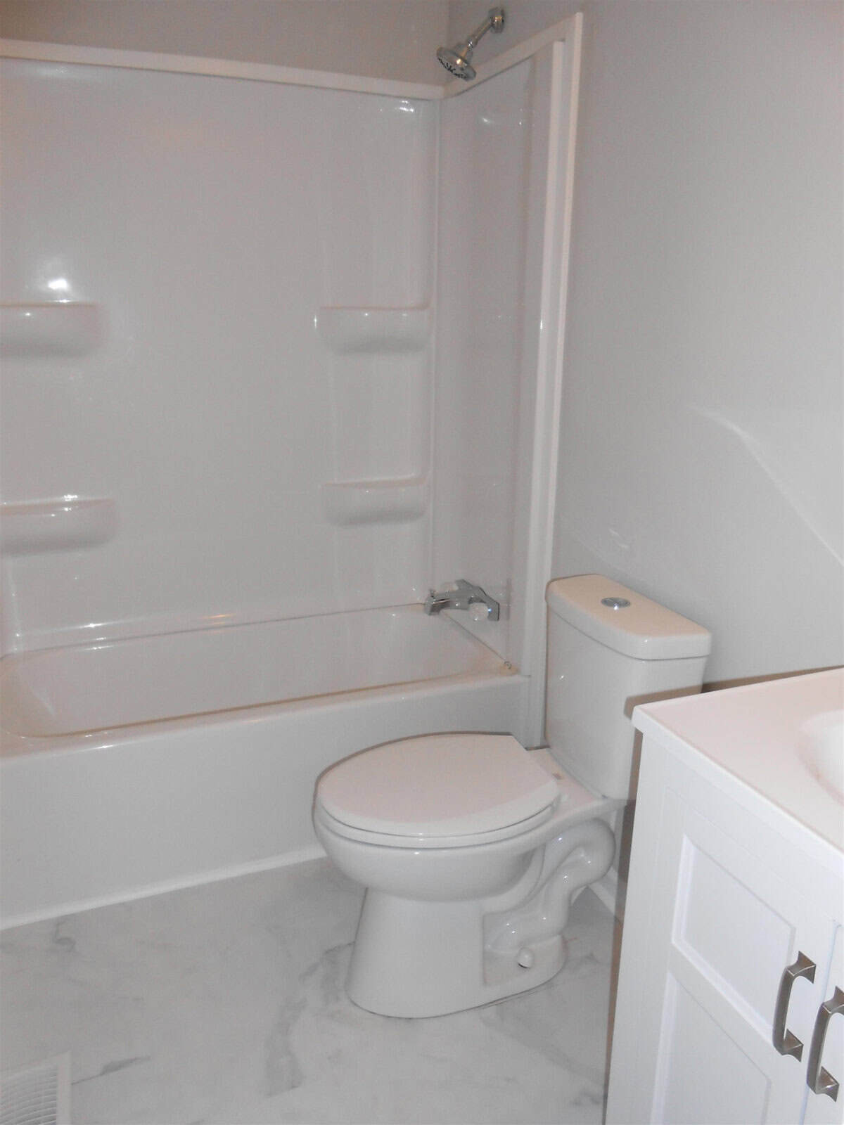 A clean, white bathroom featuring a toilet and a shower with a sliding door, set against a neutral-toned wall and floor.